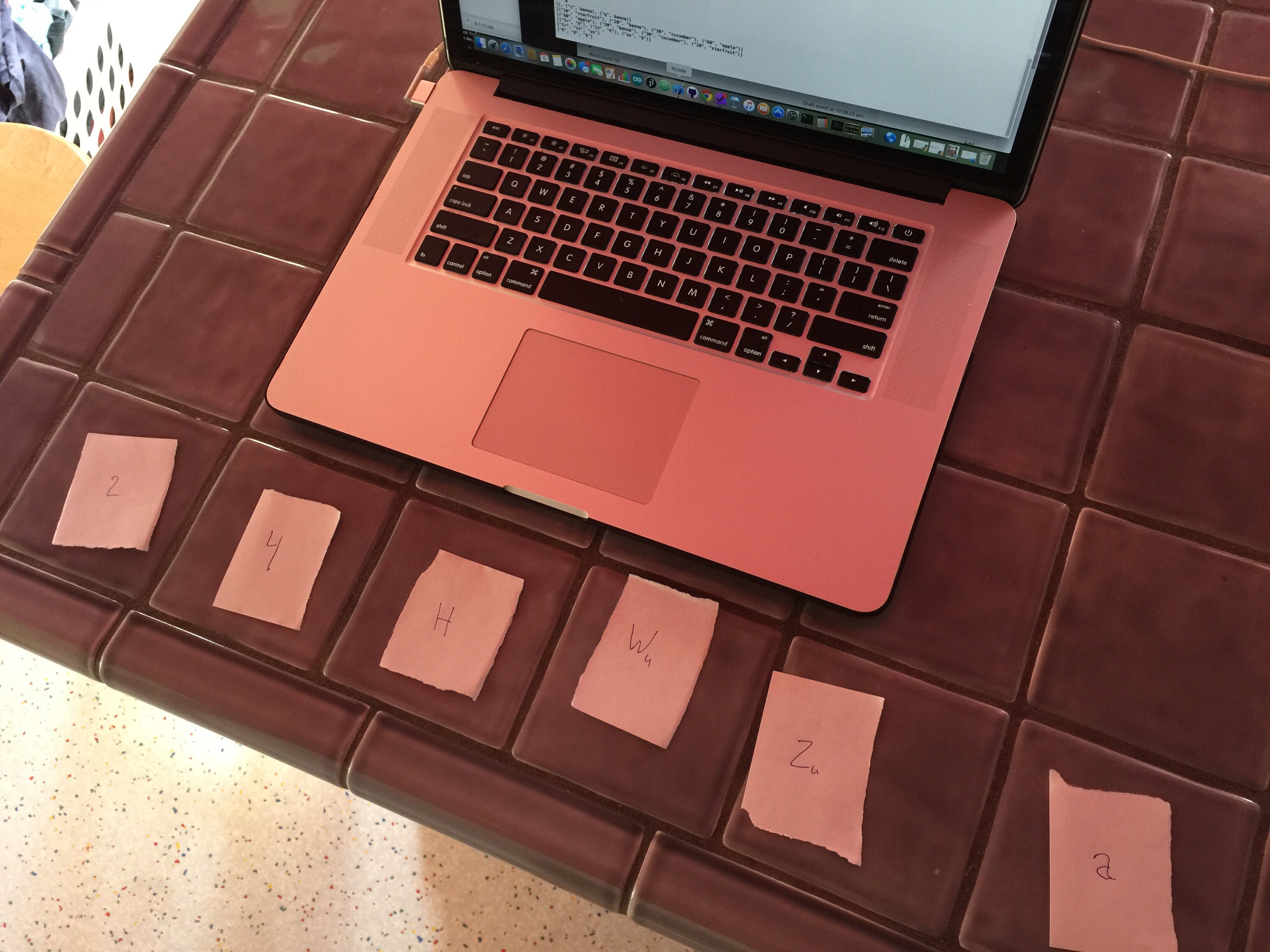 Laptop computer on kitchen counter with small pieces of paper lined up in a row.